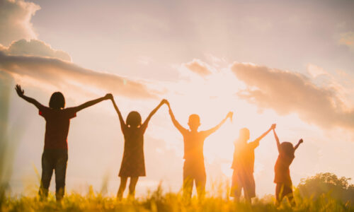 Silhouette von Kindern die zusammen ihre Arme beim Sonnenuntergang heben